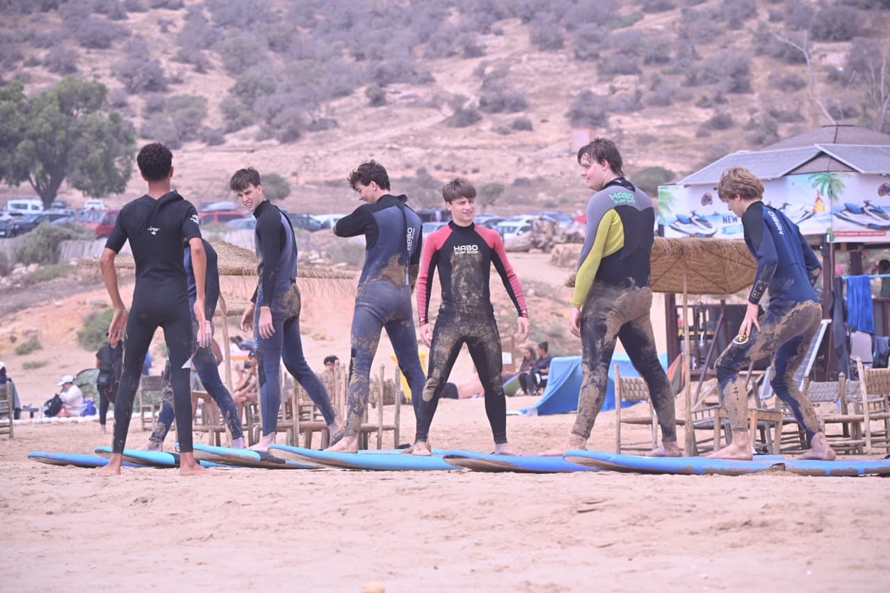 Surfers in wetsuits gathered with their boards on the sand at Taghazout in warm Atlantic light